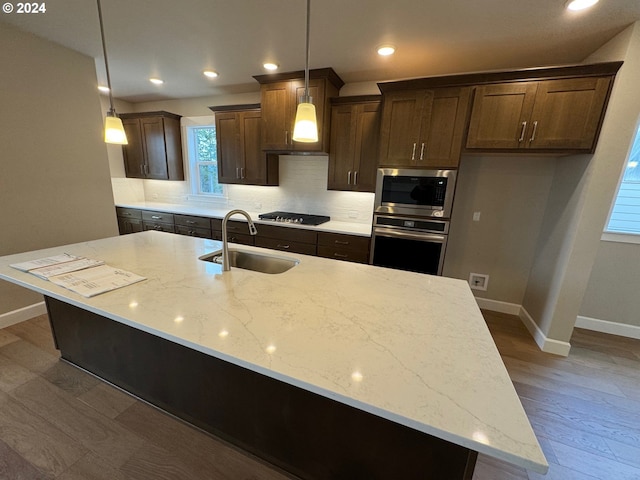 kitchen with light stone countertops, sink, dark wood-type flooring, pendant lighting, and appliances with stainless steel finishes