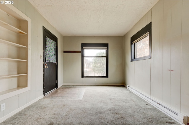 carpeted spare room featuring built in shelves, a baseboard heating unit, wooden walls, and a textured ceiling