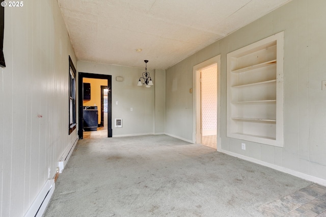 carpeted empty room featuring a baseboard heating unit, a chandelier, and built in shelves