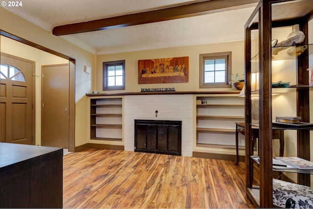 foyer entrance featuring hardwood / wood-style floors, beamed ceiling, a textured ceiling, and a brick fireplace