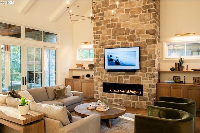 living room featuring hardwood / wood-style floors, a stone fireplace, a high ceiling, a notable chandelier, and beamed ceiling