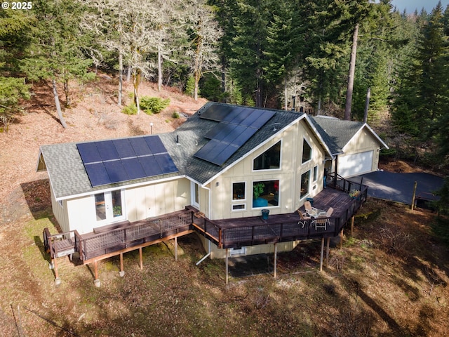 back of house with a deck, board and batten siding, roof with shingles, and roof mounted solar panels