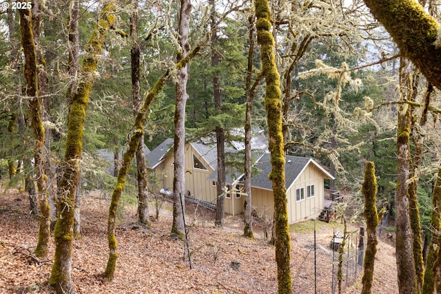 view of side of property with a wooded view, board and batten siding, and roof with shingles