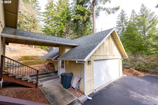 view of side of home with a detached garage, roof with shingles, and board and batten siding