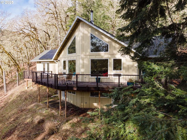 rear view of house with roof mounted solar panels and a deck