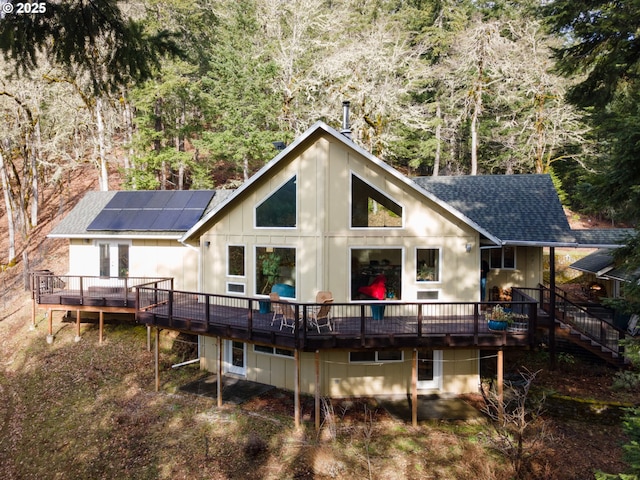 back of house featuring a wooden deck, roof mounted solar panels, and a shingled roof