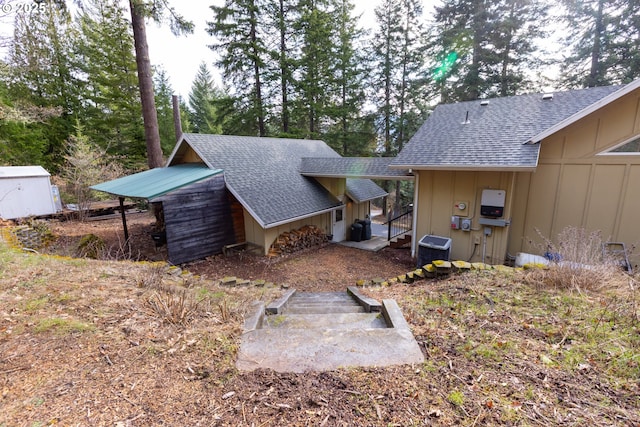 rear view of property with central air condition unit, board and batten siding, and roof with shingles