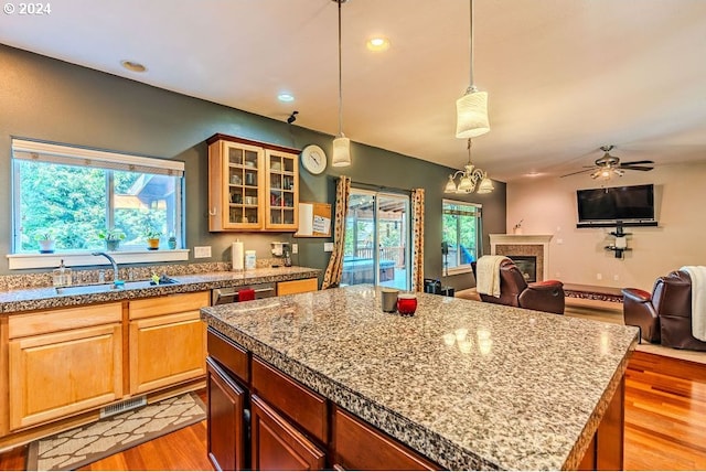 kitchen with a tile fireplace, decorative light fixtures, light hardwood / wood-style floors, ceiling fan, and a kitchen island