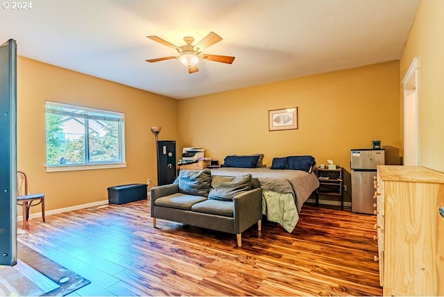 bedroom featuring stainless steel fridge, wood-type flooring, and ceiling fan