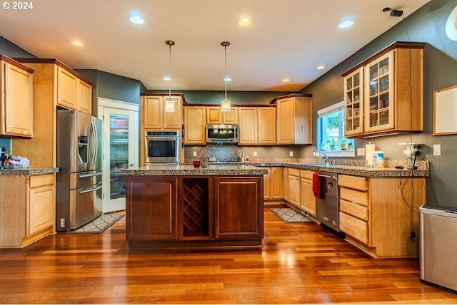 kitchen featuring decorative light fixtures, wood-type flooring, an island with sink, sink, and appliances with stainless steel finishes