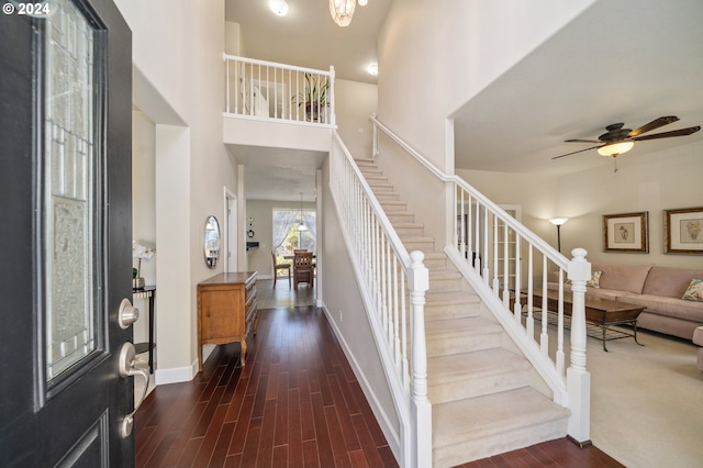 foyer entrance with a high ceiling, ceiling fan with notable chandelier, and dark hardwood / wood-style flooring