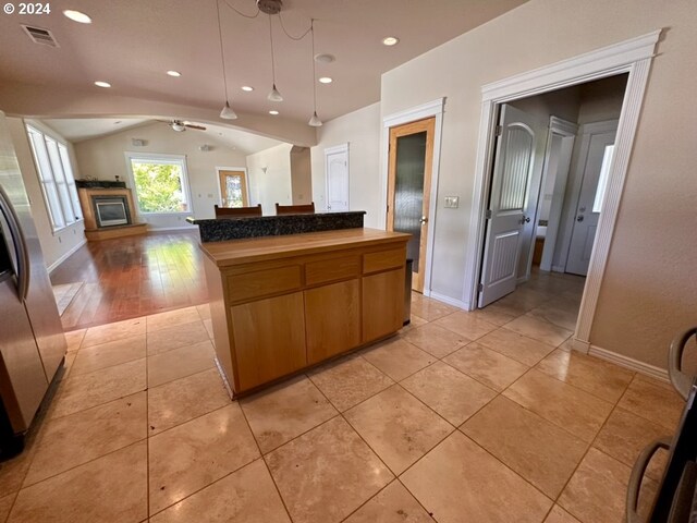 kitchen with stainless steel refrigerator with ice dispenser, light tile patterned flooring, a center island, vaulted ceiling, and pendant lighting