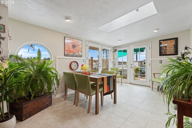 tiled dining room featuring vaulted ceiling with skylight, french doors, and a textured ceiling