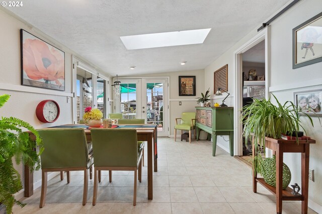 dining area featuring vaulted ceiling with skylight, light tile patterned floors, a textured ceiling, and french doors