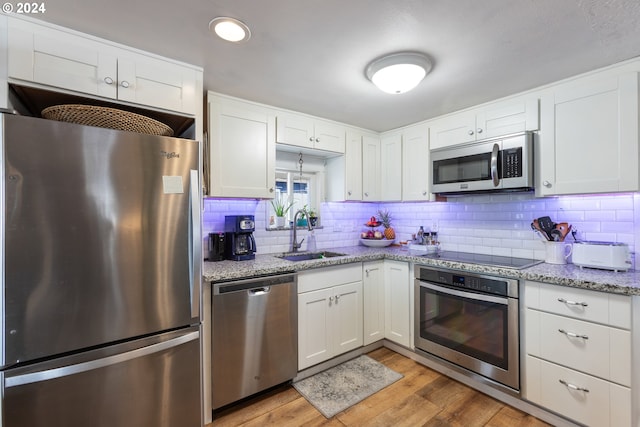 kitchen with appliances with stainless steel finishes, white cabinetry, sink, backsplash, and light wood-type flooring