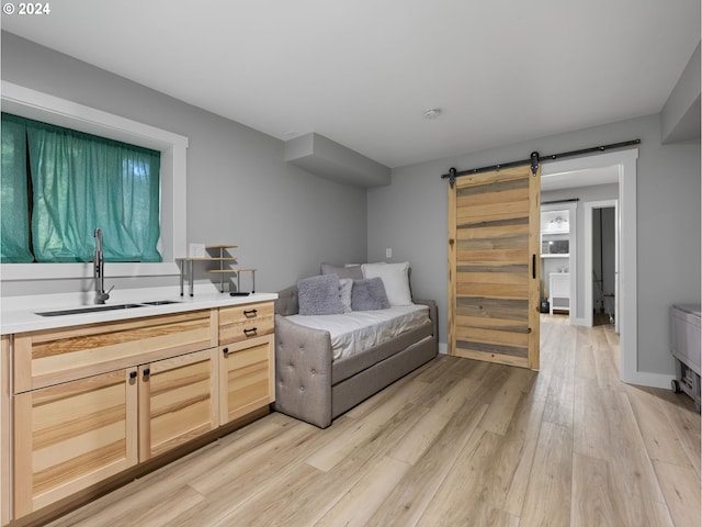 bedroom with a barn door, sink, and light wood-type flooring