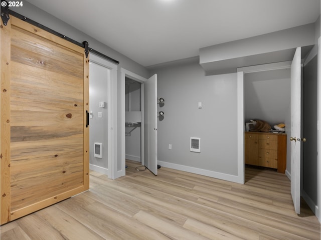 unfurnished bedroom with a barn door and light hardwood / wood-style flooring