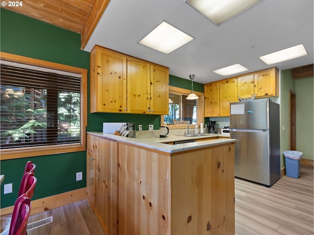 kitchen with stainless steel fridge, hanging light fixtures, light wood-type flooring, kitchen peninsula, and light brown cabinets