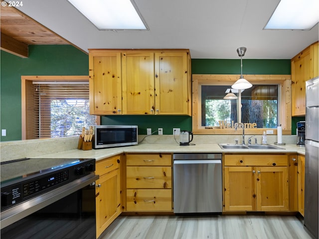 kitchen with a skylight, sink, hanging light fixtures, stainless steel appliances, and light hardwood / wood-style flooring