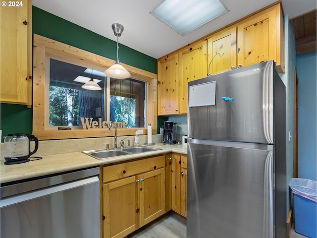 kitchen featuring appliances with stainless steel finishes, sink, light hardwood / wood-style floors, and decorative light fixtures