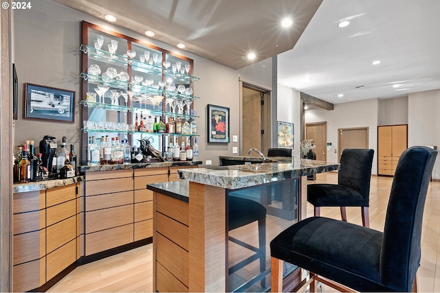 bar with light brown cabinetry, light hardwood / wood-style floors, and stone countertops