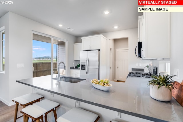 kitchen with stainless steel appliances, recessed lighting, white cabinets, a sink, and a peninsula