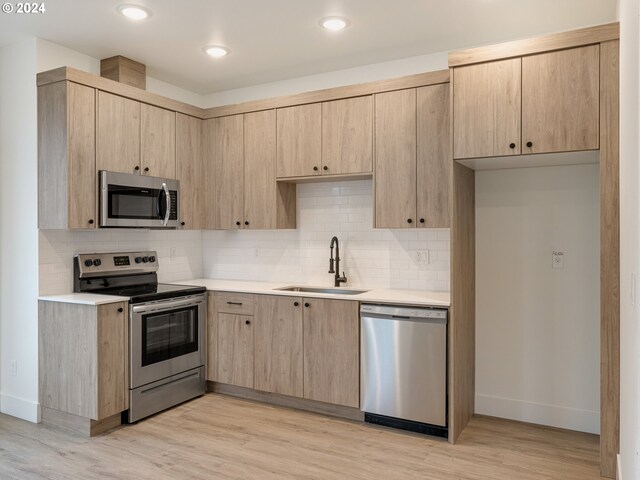 kitchen featuring appliances with stainless steel finishes, light brown cabinetry, sink, decorative backsplash, and light wood-type flooring