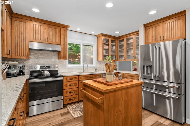 kitchen with stainless steel appliances, decorative backsplash, sink, light hardwood / wood-style flooring, and a center island