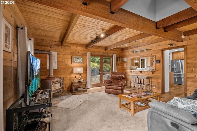 carpeted living room featuring wooden ceiling, a wood stove, wood walls, and beamed ceiling