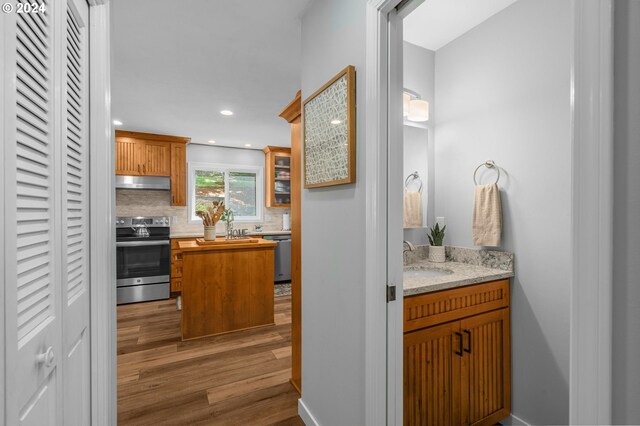 kitchen featuring decorative backsplash, appliances with stainless steel finishes, sink, light hardwood / wood-style flooring, and light stone counters