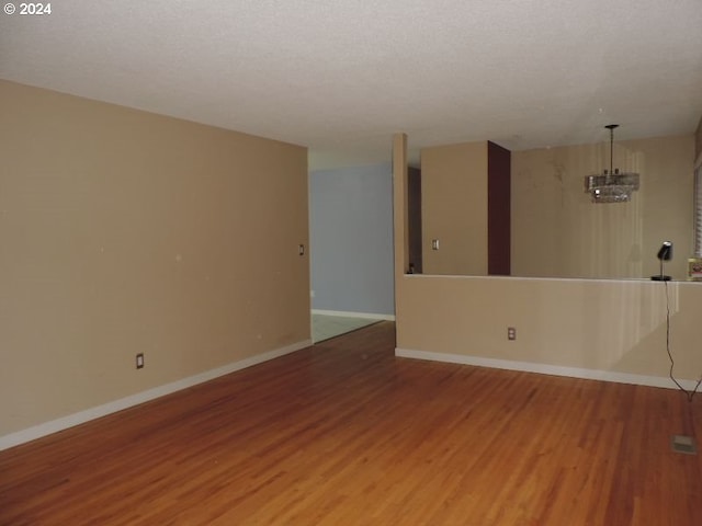 spare room with a notable chandelier, wood-type flooring, and a textured ceiling