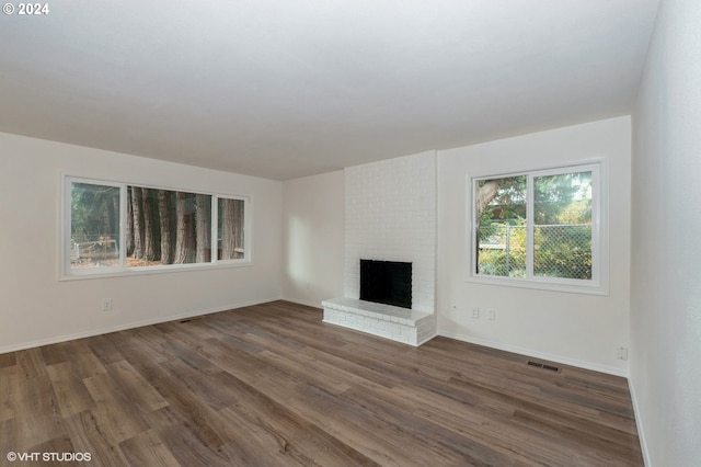 unfurnished living room with dark hardwood / wood-style flooring and a brick fireplace