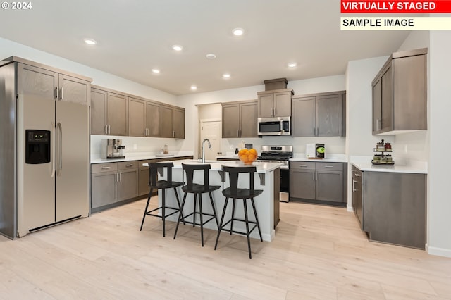 kitchen featuring a center island with sink, a breakfast bar area, appliances with stainless steel finishes, and light hardwood / wood-style flooring