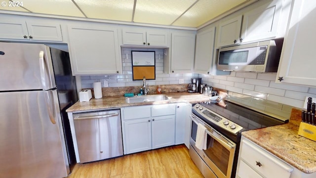 kitchen featuring sink, light stone countertops, white cabinets, light wood-type flooring, and appliances with stainless steel finishes