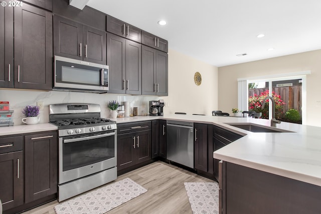 kitchen featuring kitchen peninsula, dark brown cabinetry, stainless steel appliances, sink, and light hardwood / wood-style floors