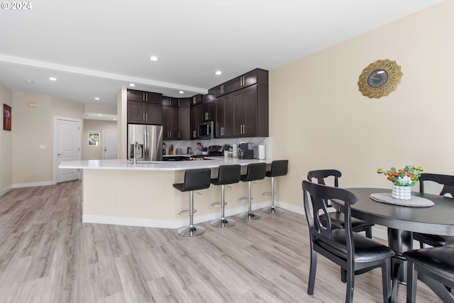 kitchen featuring dark brown cabinetry, kitchen peninsula, light hardwood / wood-style floors, a breakfast bar area, and appliances with stainless steel finishes