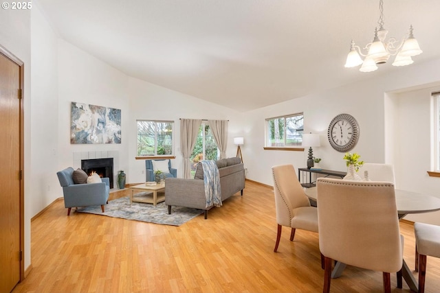 living room featuring vaulted ceiling, a notable chandelier, a fireplace, and light wood finished floors