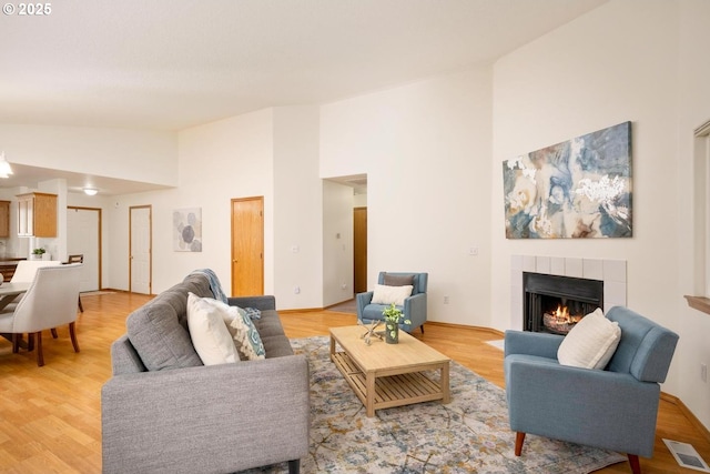 living room featuring light wood-style flooring, a fireplace, visible vents, and high vaulted ceiling