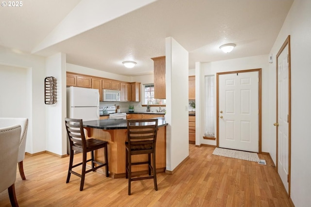 kitchen featuring a kitchen bar, dark countertops, white appliances, light wood-style floors, and baseboards