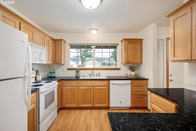 kitchen featuring white appliances, dark stone counters, light wood-style flooring, a sink, and a textured ceiling