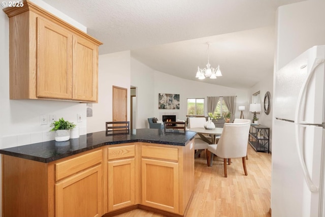 kitchen featuring light wood finished floors, a warm lit fireplace, freestanding refrigerator, a notable chandelier, and open floor plan