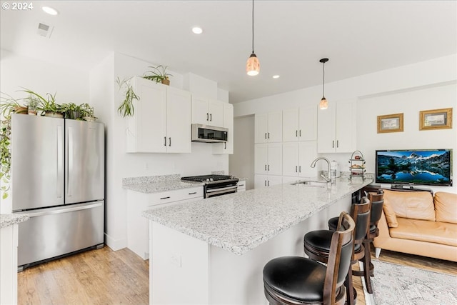 kitchen with light hardwood / wood-style floors, pendant lighting, light stone counters, and stainless steel appliances