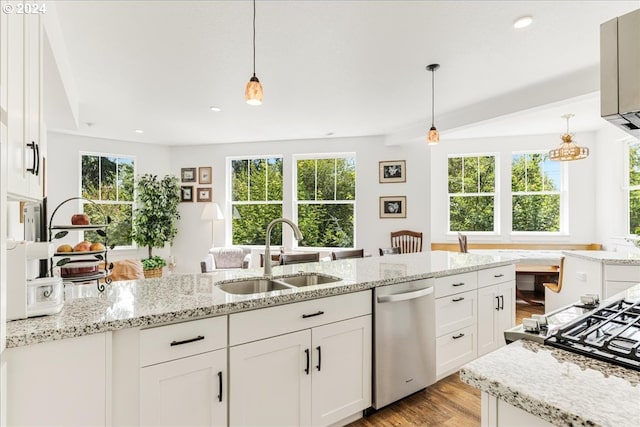 kitchen with stainless steel dishwasher, hanging light fixtures, white cabinets, light wood-type flooring, and sink