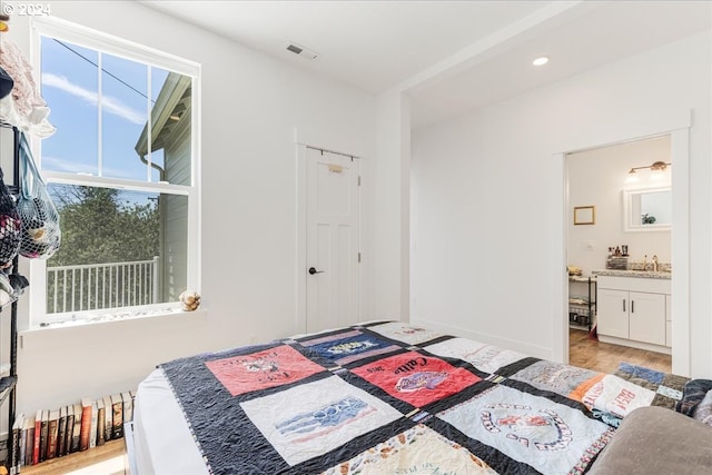 bedroom with ensuite bathroom, sink, and light wood-type flooring