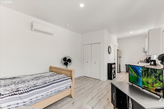 bedroom featuring a wall unit AC, a closet, stainless steel refrigerator, and light hardwood / wood-style floors