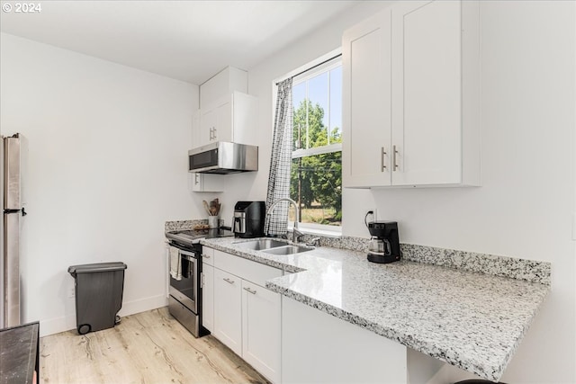 kitchen with stainless steel stove, sink, light hardwood / wood-style floors, light stone countertops, and white cabinetry