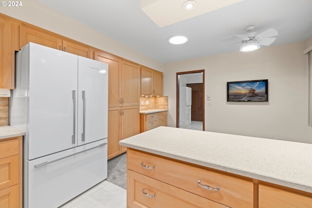 kitchen featuring light brown cabinets, backsplash, white refrigerator, ceiling fan, and light stone countertops