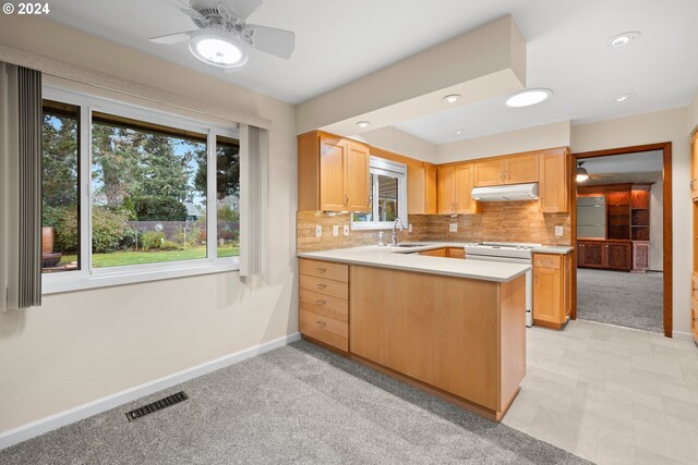 kitchen with decorative backsplash, kitchen peninsula, light carpet, light brown cabinetry, and white stove