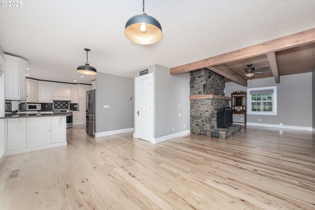 kitchen with light wood-type flooring, appliances with stainless steel finishes, white cabinetry, beamed ceiling, and open floor plan