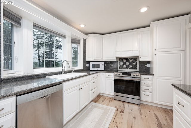 kitchen featuring light wood-style flooring, a sink, tasteful backsplash, appliances with stainless steel finishes, and white cabinets